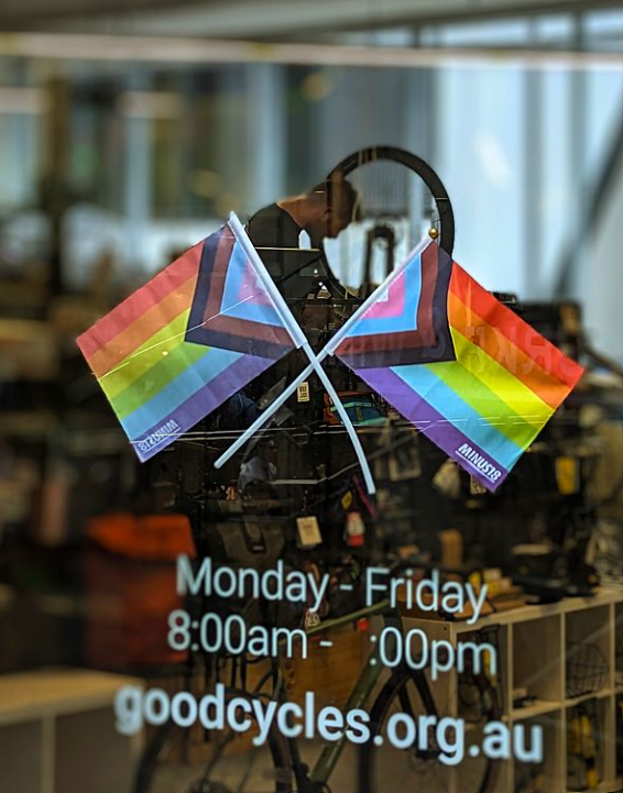 Rainbow flags attached to Goldie store front window, with bike mechanic Leigh working in the background of the photo.